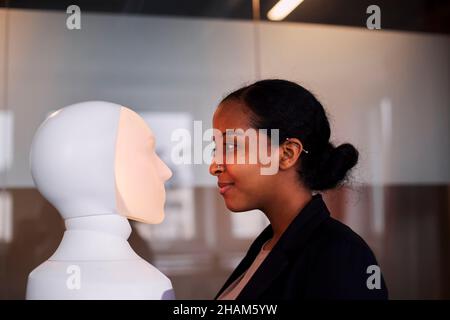 Giovane donna che guarda l'assistente vocale del robot Foto Stock