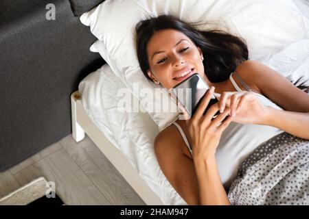 Tecnologia, internet, comunicazione e concetto di persone. Donna felice che texting sullo smartphone a letto Foto Stock