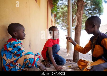 Tre ragazzi africani si siedono a terra, scherzano in giardino all'aperto per giocare a giochi divertenti Foto Stock