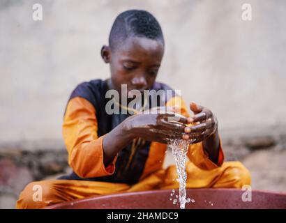 Primo piano ritratto di giovane africano ragazzo godere e giocare con acqua fresca pulita da secchio all'aperto Foto Stock