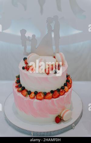 Torta nuziale tradizionale e decorativa al ricevimento di nozze. Torta nuziale bianca su più livelli su base argento e fiori rosa sulla sommità. Immagine di un Foto Stock