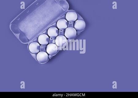 Uova bianche di pollo, 10 pezzi in una scatola di cartone nell'angolo in alto a sinistra su uno sfondo molto peri lavanda con spazio per il testo, spazio copia. Concetto - prodotti pubblicitari, Foto Stock