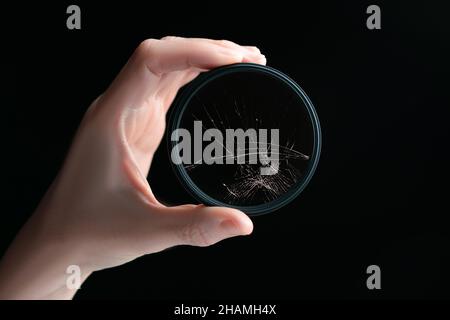 Closeup studio scatto di mano che tiene nero filtro polarizzatore circolare con vetro incrinato, isolato su sfondo nero. Concetto per danni all'ingranaggio fotografico Foto Stock
