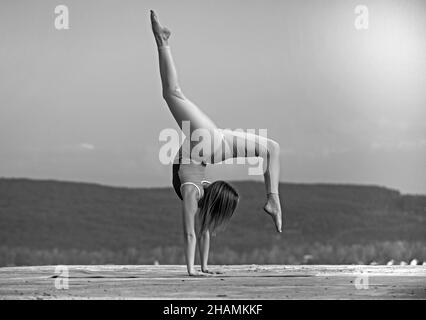 Bella donna atletica si allunga e fa un ponte sullo sfondo del cielo. Foto Stock