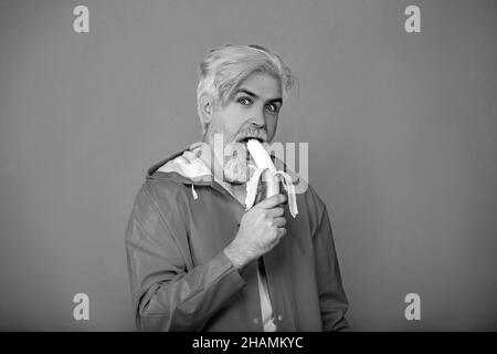 Giovane uomo serio con barba mangia banana gialla isolata su sfondo giallo. Foto Stock