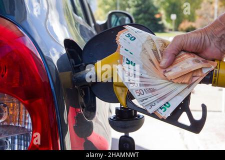 Illustrazione dell'aumento dei prezzi delle pompe. Qualcuno che riempe un serbatoio di benzina in una stazione di servizio. È in possesso di una pompa benzina e di un pacchetto di 50 euro bancari Foto Stock