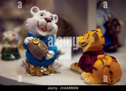 Giocattoli di Capodanno. Figurine bianco leone cucciolo Piggy banca con un barile di denaro nelle sue mani in un maglione blu e una figurina di un cub leone rosso in un sw rosso Foto Stock