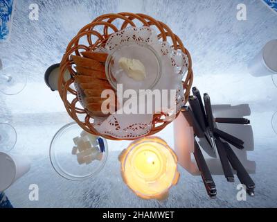 pane e burro in cestino con zucchero a cubo molti coltelli e forchette con candele pronti per il pranzo su una vera e propria tavola di scultura di ghiaccio in ristorante di ghiaccio Foto Stock