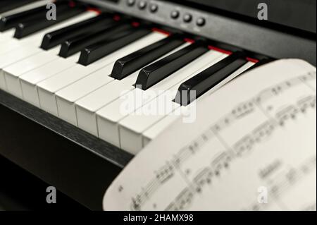 primo piano dei tasti elettronici del pianoforte. foglio di carta con note musicali. Foto Stock