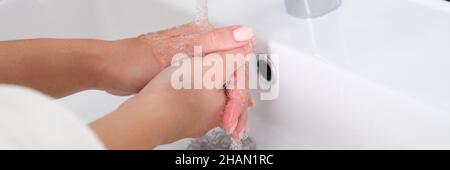 La donna lava le mani sotto l'acqua corrente nel lavabo in primo piano Foto Stock