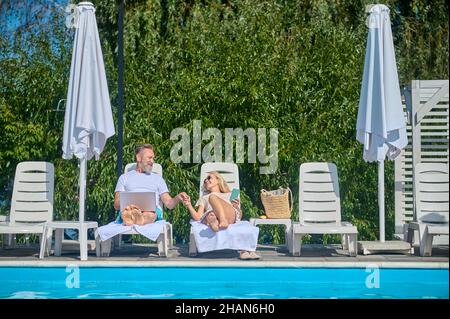 Due persone sedute su sedie a sdraio vicino alla piscina Foto Stock