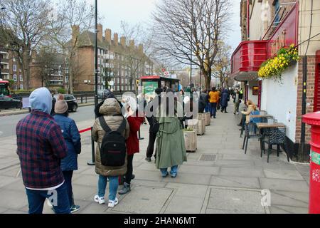 una lunga fila di persone si accaparrano per la vaccinazione di richiamo covid 19 su holloway road a nord di londra inghilterra regno unito dicembre 2021 Foto Stock