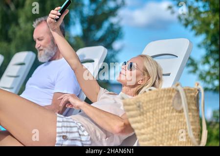 Una donna bionda seduta in un salotto chais e fare selfie Foto Stock