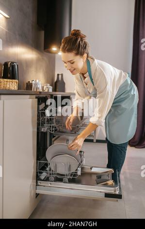 Donna in piedi vicino alla lavastoviglie ed estrarre le piastre Foto Stock