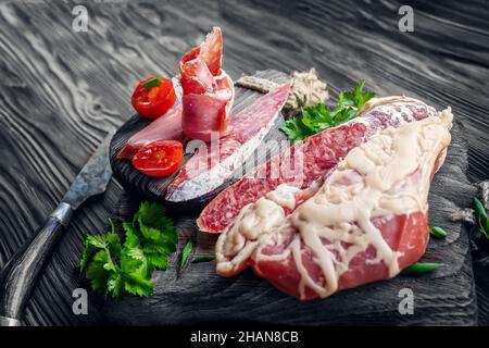 grande pezzo di carne secca in una sottile maglia di grasso interno. Un pezzo di carne fresca affumicata giace sulle foglie di spinaci. Filetto di carne di cervo naturale con Foto Stock