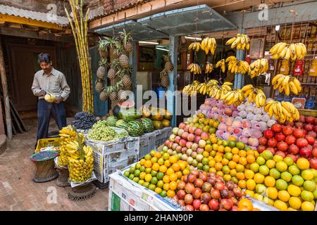 Un negoziante carves un ananas al suo stand sul lato della strada vendendo frutta fresca nella città medievale di Bhaktapur, Nepal. Foto Stock