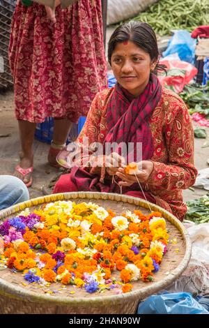 Una giovane donna nepalese che fa ghirlande di fiori per le offerte religiose ai templi indù a Kathmandu, Nepal. Foto Stock