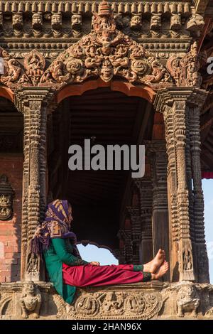 Una donna nepalese in abito tradizionale si siede di fronte al Tempio Harishankar, un tempio indù in Piazza Durbar, Patan, Nepal. Foto Stock
