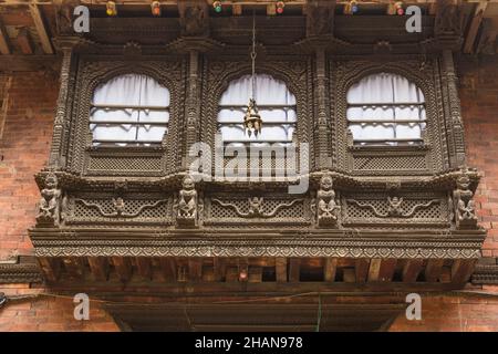 Un balcone di legno intagliato intricatamente che raffigura figure dalla mitologia indù su una residenza medievale a Patan, Nepal. In figura sono raffigurati Garuda con il Nag Foto Stock