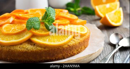 Torta di polenta all'arancia e mandorla decorata con fette di arancia candita e tangerini su vecchio sfondo di legno. Torta di polenta capovolta. Torta fatta in casa w Foto Stock