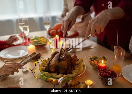 Uomo anziano irriconoscibile che taglia il tacchino di Natale arrostito, celebrando il Natale con la sua famiglia di multi generazione a casa Foto Stock