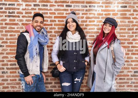 Positivo multirazziale giovani amici maschili e femminili indossando abiti casual trendy in piedi vicino a muro di mattoni e sorridendo alla macchina fotografica Foto Stock