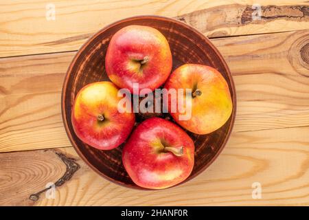 Quattro mele rosse dolci in un piatto di argilla su un tavolo di legno, primo piano, vista dall'alto. Foto Stock