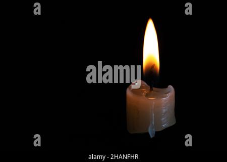 Su uno sfondo nero, la luce brillante della candela brucia in basso Foto Stock