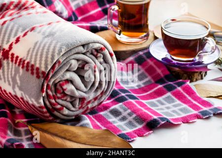 Coperta in pile grigio arrotolata su coperta rosa con due tazze di tè e foglie d'autunno. Foto Stock