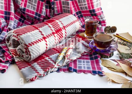 Coperta di pile grigio arrotolata su una coperta rosa su terreno bianco con due tazze di tè turco tradizionale e foglie d'autunno. Foto Stock