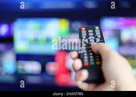 Telecomando in mano femmina sullo sfondo dello schermo Smart TV. Donna che sceglie i servizi di streaming, guardando i film Foto Stock