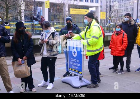 Manchester, Regno Unito, 14th dicembre 2021. Un uomo in hi vis dal centro di vaccinazione del municipio dice alle persone in coda che non hanno abbastanza vaccini per vaccinare quelli in coda oltre il segno nell'immagine e stanno cercando di ottenere più vaccini. Le persone sono in coda per un vaccino di richiamo per proteggere contro Covid-19 o Covid o Coronavirus presso il Municipio di Manchester, Inghilterra, Regno Unito. Il governo del Regno Unito ha annunciato un programma di vaccinazione di richiamo di massa contro la variante Omicron Covid. Credit: Terry Waller/Alamy Live News Foto Stock