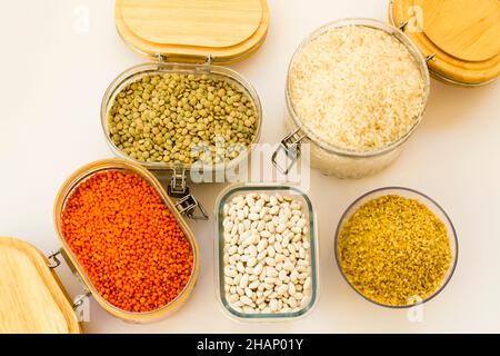 Gruppo di alimenti a base di cereali secchi non cotti in contenitori di vetro bianchi, vista dall'alto Foto Stock