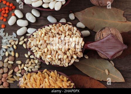 Gruppo di alimenti a base di cereali secchi non cotti in cucchiai di legno su superficie di legno con foglie autunnali, concetto di raccolta Foto Stock