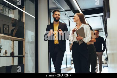 Giovani professionisti che hanno una discussione in un ufficio moderno. Due giovani uomini d'affari sorridenti mentre camminano insieme in un corridoio. Allegro colle Foto Stock