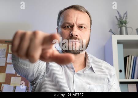 Indice dell'uomo di Medio Evo serio che punta alla macchina fotografica nell'ufficio domestico. Ho scelto il concetto di gesto. Foto Stock