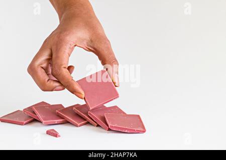 Il quarto tipo di cioccolato: Cioccolato al rubino affettato e con una mano che tiene un pezzo su sfondo bianco con spazio copia Foto Stock