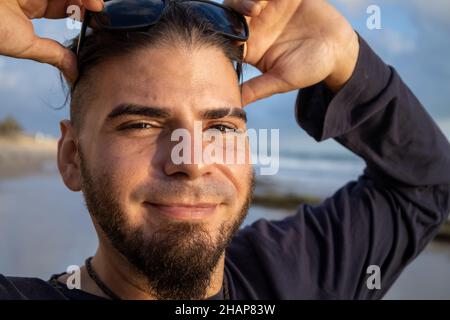 Giovane uomo di hipster o hippie aspetto con viso felice sulla spiaggia Foto Stock