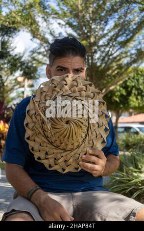 Uomo adulto con l'aspetto hippy o hippie guardando seriamente la macchina fotografica mentre si copre con un cappello di paglia rustico. Aspetto maleducato o arrabbiato. Foto Stock