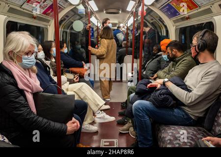 Londra, Regno Unito. 14 dicembre 2021. Le persone viaggiano con la metropolitana della linea Bakerloo alle 4pm, poco prima dell'ora di punta, la maggior parte delle quali indossa una copertura facciale in conformità con il requisito del governo britannico di farlo sui trasporti pubblici. Il secondo giorno del piano del governo di combattere la diffusione della variante di Omicron, il “piano B”, attualmente in discussione alla Camera dei Comuni, e la raccomandazione di lavorare da casa, il tubo è inaspettatamente occupato. Credit: Stephen Chung / Alamy Live News Foto Stock