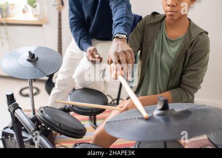 Insegnante maschile africano che spiega la scolaretta biraciale con i bastoncini da batteria come giocare a drumkit a casa lezione Foto Stock