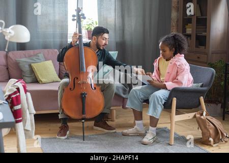 Giovane insegnante sicuro di musica che interagisce con la scolgirl diligente facendo appunti mentre lo ascolta Foto Stock