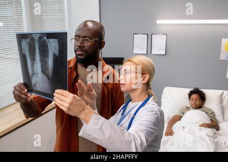 Medico femminile che mostra l'immagine radiografica dei polmoni al padre, e discutono la malattia insieme in ospedale Foto Stock