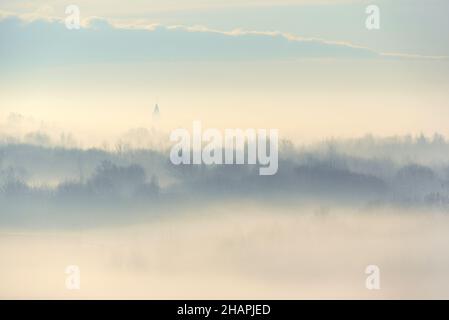 Profili di alberi e chiesa nella nebbia strisciando. Paesaggio invernale Foto Stock