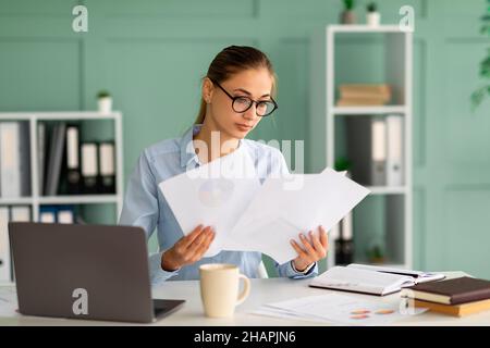 Donna d'affari concentrata che lavora con rapporti e documenti, seduto con il laptop sul posto di lavoro all'interno dell'ufficio Foto Stock