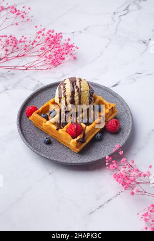 Waffle belgi con bacche gelato e fiori sul verde Foto Stock