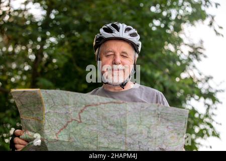 Uomo anziano che guarda alla mappa durante la sua gita in bicicletta o in bicicletta nella foresta, concetto di stile di vita sano Foto Stock