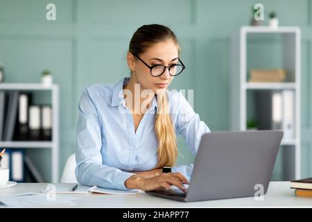 Donna d'affari millenaria che lavora con il computer portatile alla scrivania in ufficio, imprenditore femminile che digita documento Foto Stock