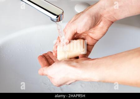 Lavando le mani con sapone sotto l'acqua corrente nel bagno sopra il lavandino. Concetto di igiene per la protezione contro le infezioni da coronavirus. Pulizia manuale Foto Stock
