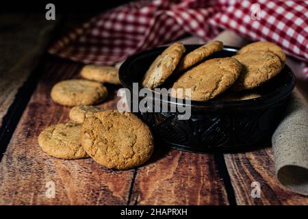 Una vista piana di un miele fatto in casa uvetta farina d'avena biscotti in una ciotola nera e su un tavolo di legno. Concetto di alimentazione naturale e sana. Foto Stock